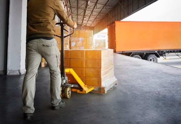 En person flyttar kartonger på en pall i ett lager med en palltruck.